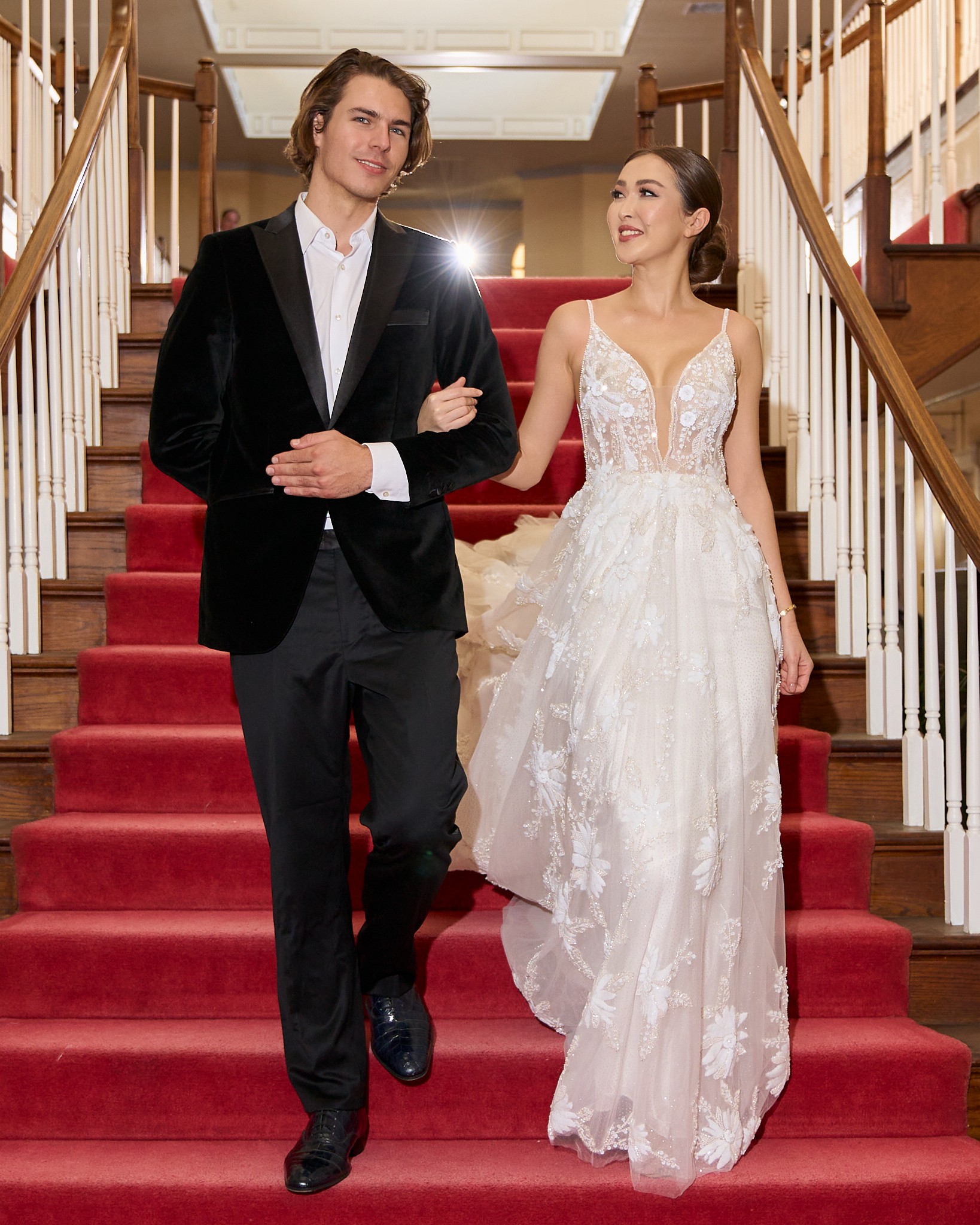 Wedding couple standing arm in arm on a red-carpeted staircase